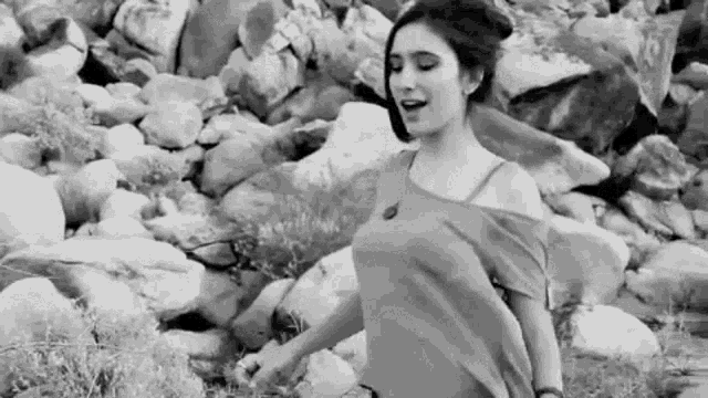 a black and white photo of a woman standing on a rocky hillside .