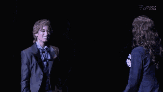 a man in a suit is standing next to a woman in a suit and the words takarazuka sky stage are on the bottom right