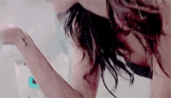 a woman with a tattoo on her arm is washing her hair in a bathroom .