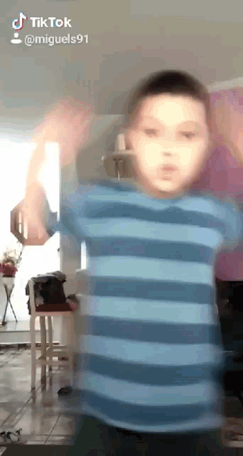 a young boy in a blue and white striped shirt is dancing in a living room