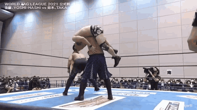 a wrestler is carrying another wrestler on his shoulders in a wrestling ring .