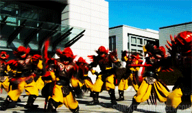a group of people in yellow and red costumes are dancing in front of a building which says chicagocityworld.com on the bottom