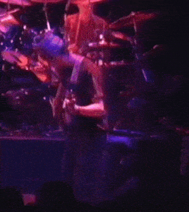 a man is playing a guitar on a stage in front of a drum set