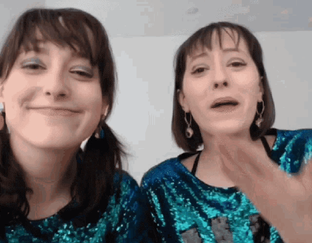 two women wearing blue sequined tops are making faces