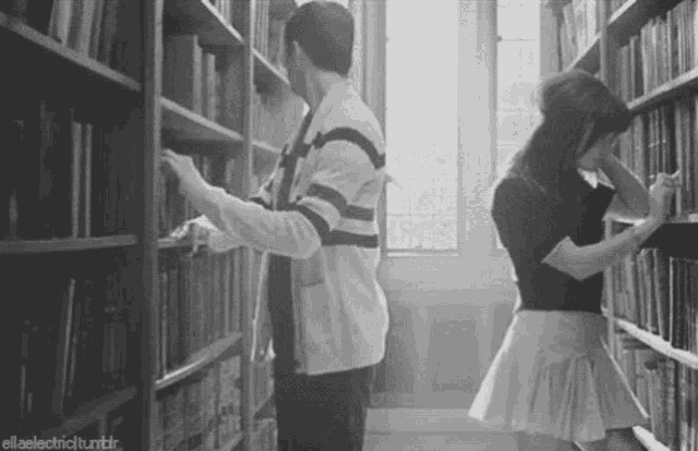 a man and a woman are in a library looking at books .