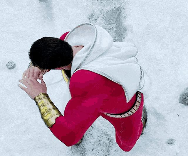 a man in a red and white superhero costume is kneeling down in the snow .