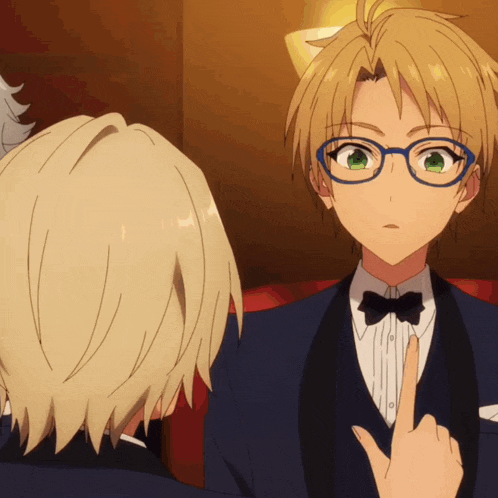 a man wearing glasses and a tuxedo points at another man