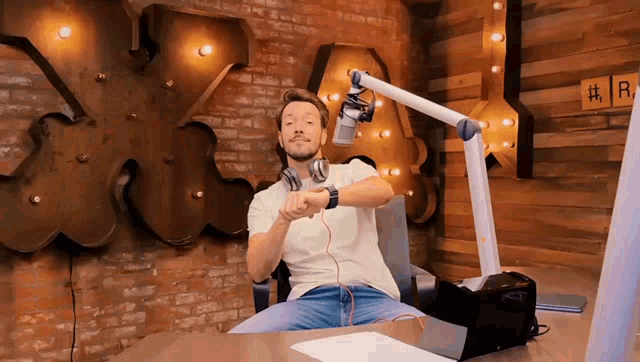 a man wearing headphones and a watch is sitting in front of a microphone in front of a sign that says # r