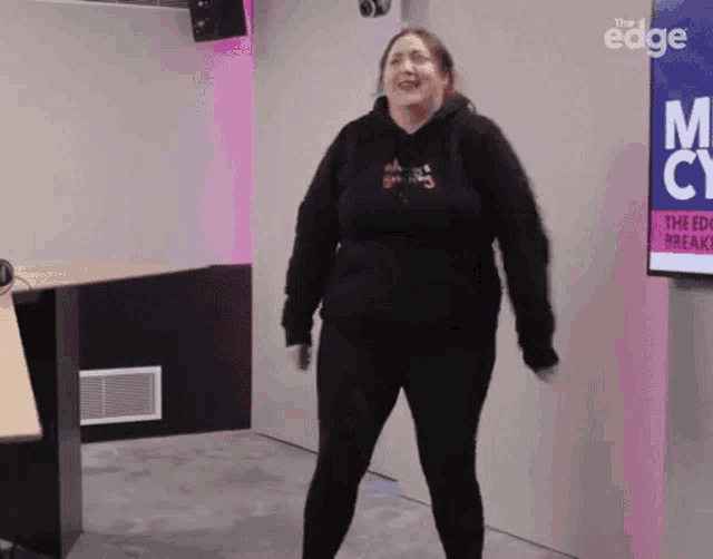a woman in a black hoodie is standing in front of a sign that says the edge on it
