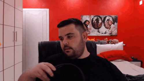 a man is sitting in a chair in front of a red wall