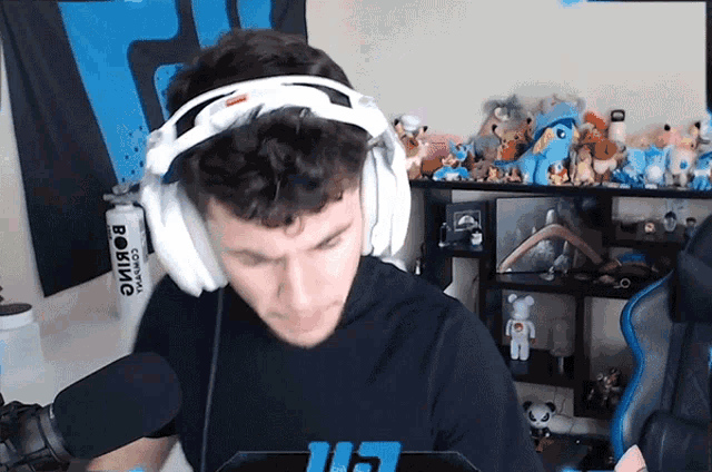 a man wearing headphones is sitting in front of a microphone in front of a shelf with stuffed animals