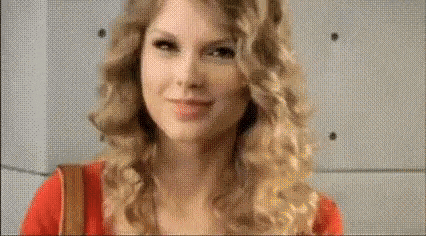 taylor swift is wearing a red shirt and a brown purse .
