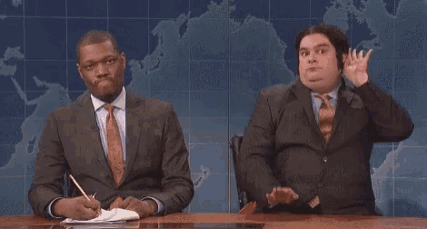 a man in a suit and tie is throwing a piece of paper in the air while sitting at a desk .