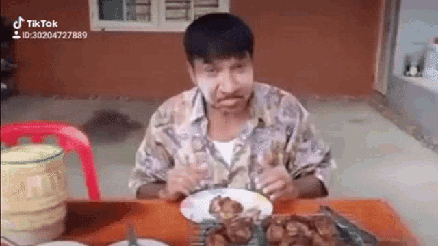 a man is sitting at a table eating food and making a face .