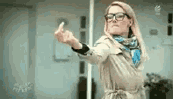 a woman with glasses and a trench coat is giving the middle finger .