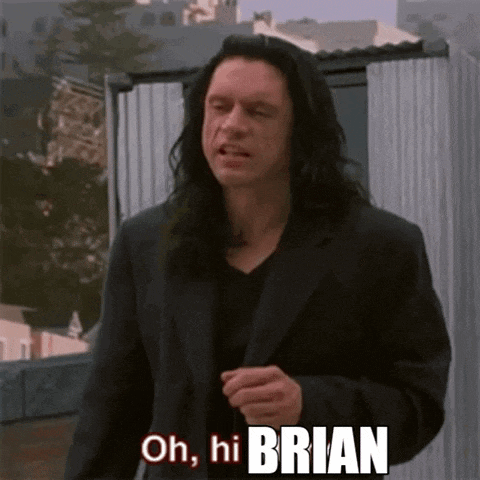 a man with long hair is standing in front of a building and saying oh hi brian