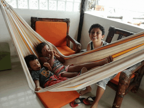 three children are laying in a hammock and one of them is wearing a shirt that says california