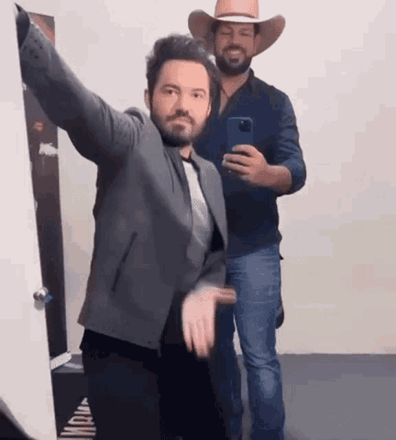a man in a cowboy hat is taking a selfie with another man in a suit .