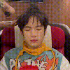 a young man is sitting in a chair with his eyes closed and a person is holding his hair .