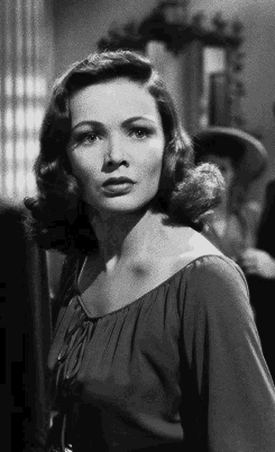 a black and white photo of a woman in a dress standing in front of a window .