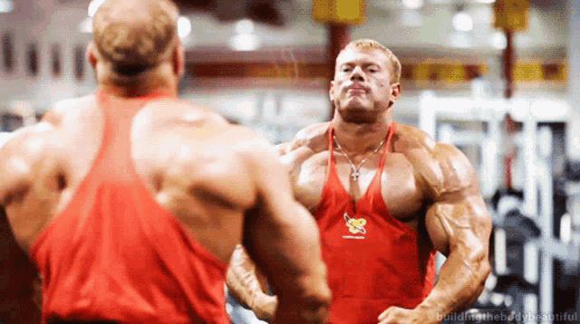 a man in a red tank top is looking at himself in a mirror