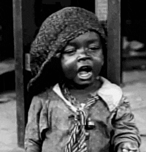 a black and white photo of a young boy wearing a hat and a tie .