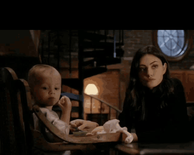 a woman is sitting at a table with a baby in a high chair
