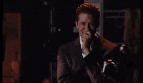 a man in a suit and tie is laughing while holding his hand to his face