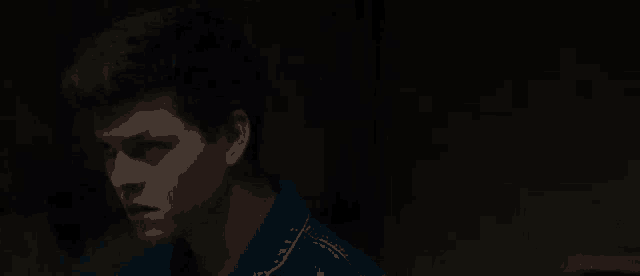 a young man in a blue denim jacket is standing in the dark .