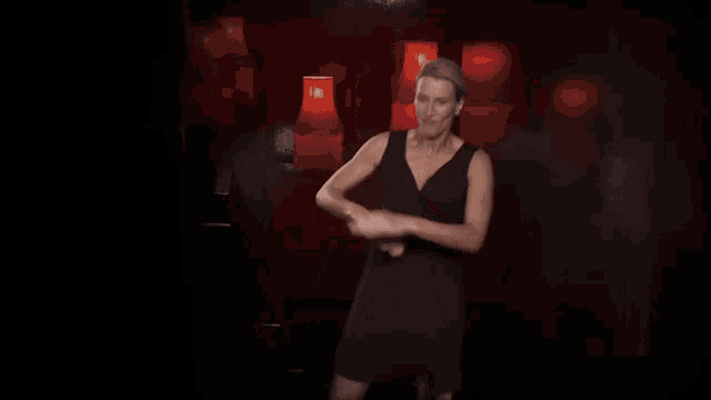a woman in a black dress is dancing in front of red lamps in a dark room .