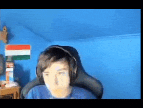 a young boy wearing headphones and a blue shirt is sitting in a gaming chair .