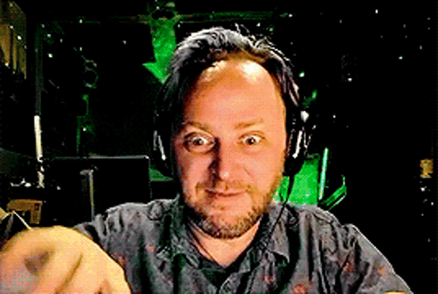 a man with a beard wearing headphones is smiling and pointing at the camera
