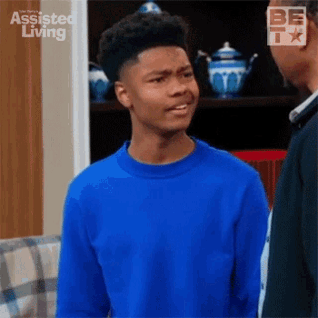 a young man in a blue sweater is standing next to a man in a black shirt and making a funny face .