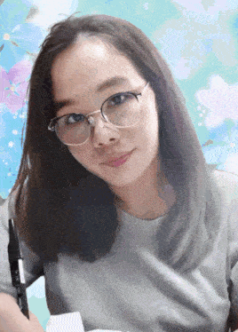 a woman wearing glasses and a gray shirt has a pen in her right hand