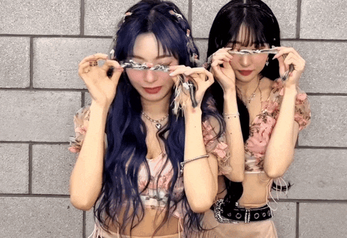 two women with blue hair are covering their eyes with a ribbon