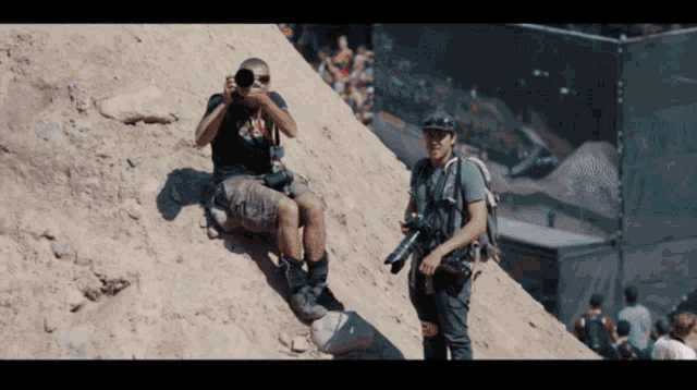 a man is taking a picture of another man sitting on a hill