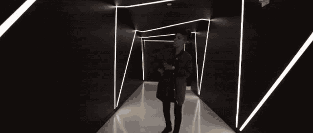 a man in a black coat stands in a dark hallway with white lights on the walls