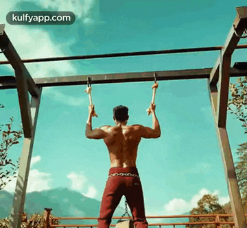 a shirtless man is doing pull ups on a bar outdoors .