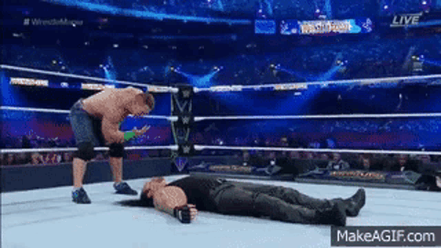 two men are wrestling in a wrestling ring and one of them is laying on the floor .