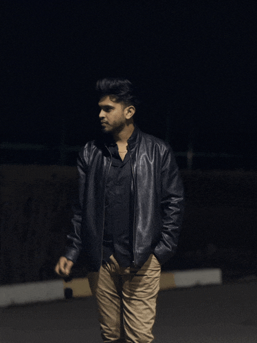 a young man wearing a black leather jacket stands in the dark
