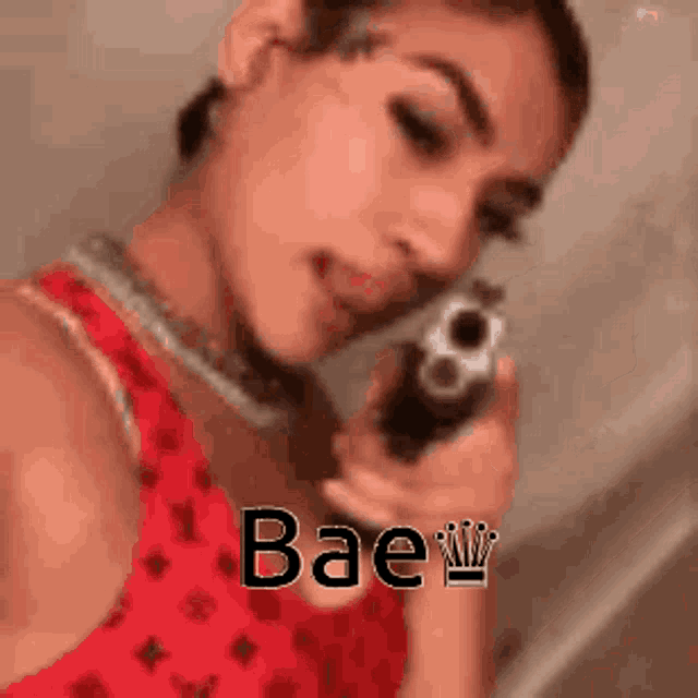a woman in a red dress is pointing a gun at the camera with the words bae written on the bottom .