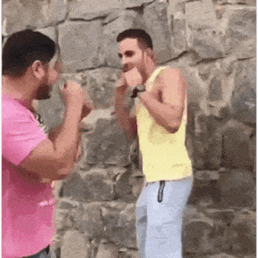 two men are fighting each other in front of a brick wall .