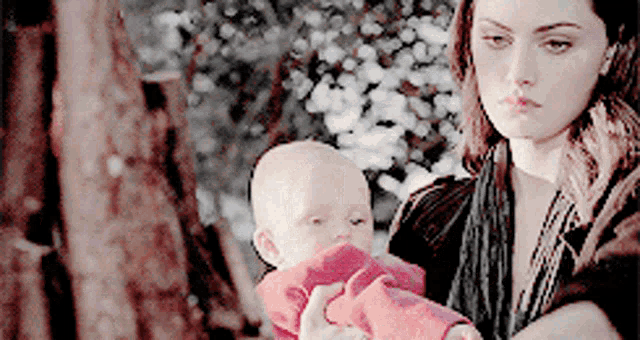 a woman is holding a baby in her arms in front of a tree