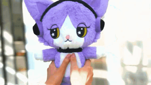a person is holding a purple stuffed cat with headphones on its head