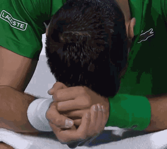 a man in a green lacoste shirt is covering his face with his hands