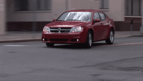 a red dodge car is driving down the street