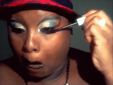a woman wearing a baseball cap is applying mascara to her eye