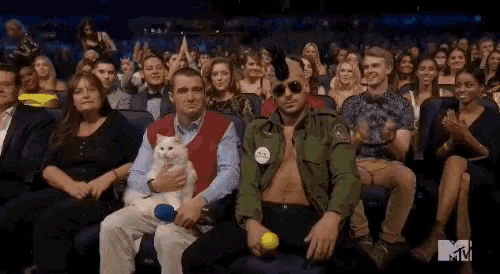 a man in a green jacket is holding a cat while sitting in the audience at a mtv event