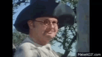 a man wearing a hat and glasses is standing in a field .