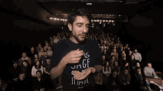 a man stands in front of a crowd wearing a shirt that says moins sage que imag